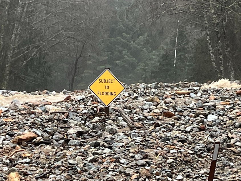caption: A "Subject to Flooding" sign is nearly covered with debris on State Route 20 near Colonial Creek on Dec. 5, 2023.