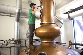 caption: Tyler Pederson, head stillman at Westland Distillery, climbs onto the still to check to see if the spirits were condensing on the still's plates on Monday, March 19, 2018, at Westland Distillery in Seattle. 