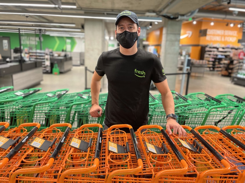 caption: Dany Curbelo poses among some of the older style shopping carts at Amazon Fresh for customers who don't want to use the smart "Dash" carts