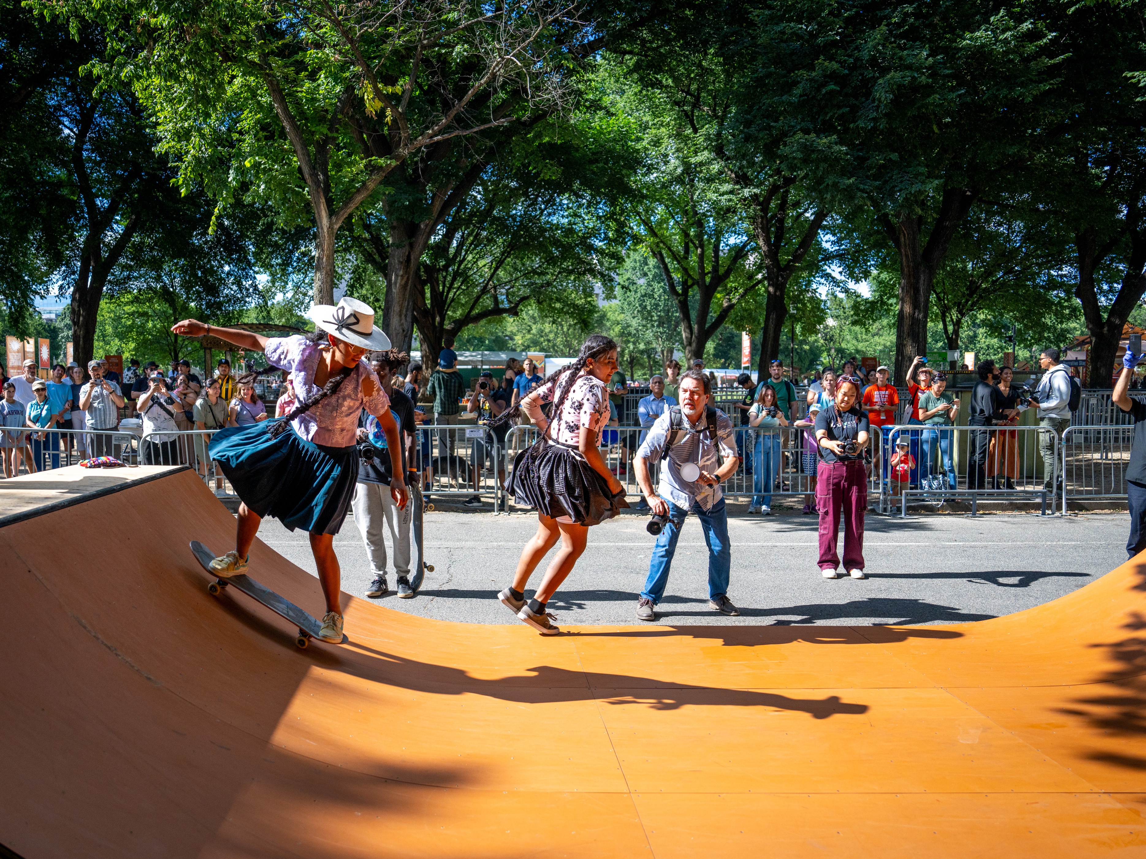 caption: Bolivian women skateboarders — wearing traditional garb — demonstrate their skills on the half pipe. 