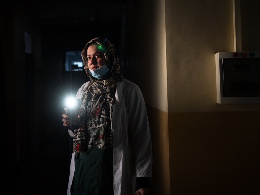 caption: Dr. Elaha Ibrahimi uses her phone as a flashlight during a power cut inside the hospital in Mirbacha Kot, Afghanistan, in October. Health care workers have continued to work without salaries, without medicine for patients and with frequent power cuts.