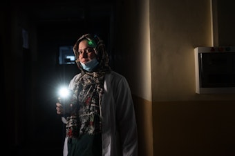 caption: Dr. Elaha Ibrahimi uses her phone as a flashlight during a power cut inside the hospital in Mirbacha Kot, Afghanistan, in October. Health care workers have continued to work without salaries, without medicine for patients and with frequent power cuts.