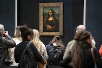 caption: Visitors observe the painting the <em>Mona Lisa</em> by Italian artist Leonardo da Vinci on display in a gallery at Louvre on May 19, 2021 in Paris, France.