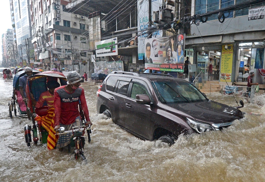 caption: Commuters make their way through a water-logged street after a heavy downpour in Dhaka. Bangladesh is one of many countries struggling to protect residents from the effects of climate change.