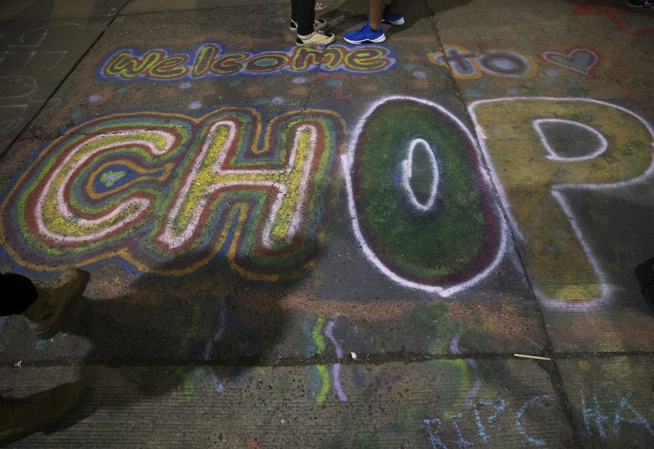 caption: Welcome to CHOP, (Capitol Hill Occupied Protest), is spray painted on the pavement at the intersection of 11th Avenue and East Pine Street on Saturday, June 13, 2020, in Seattle. 