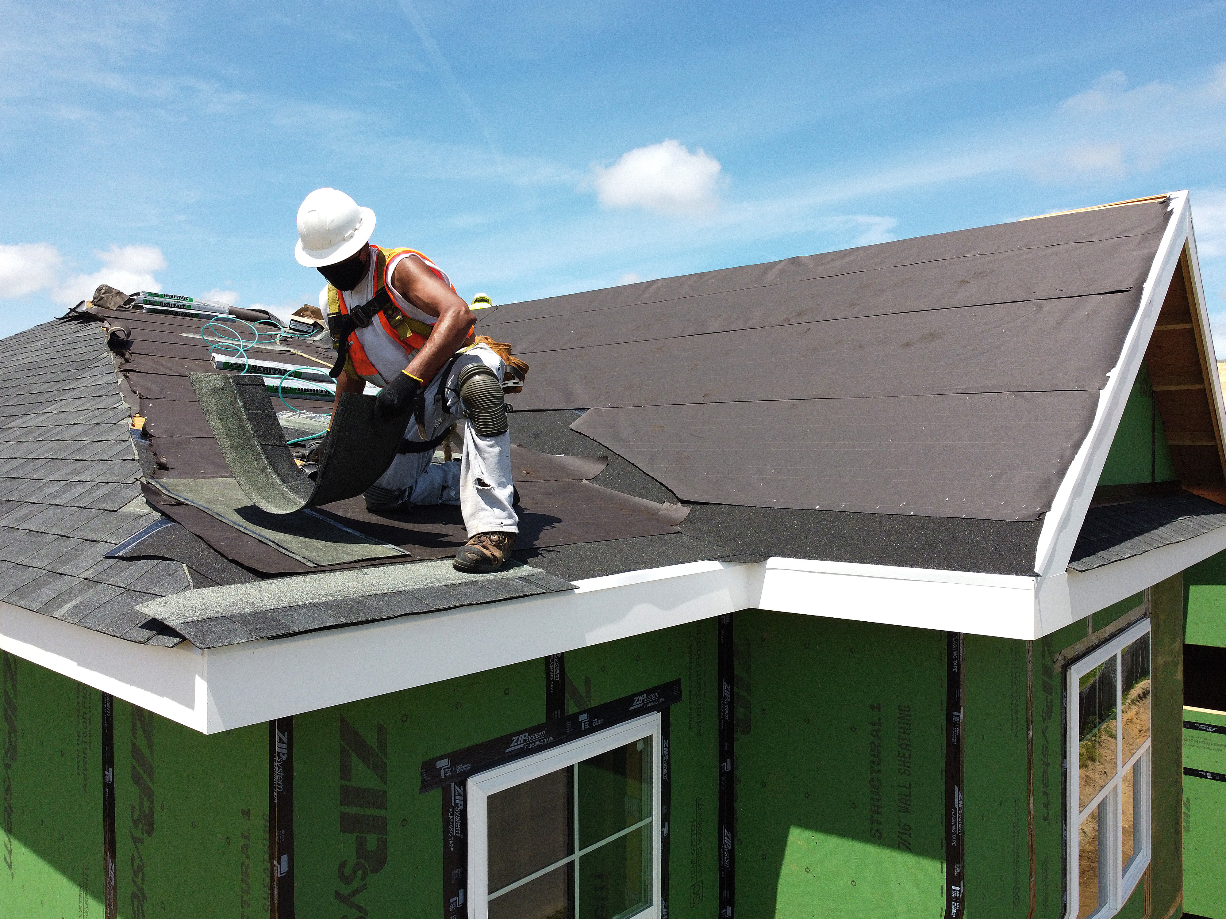 caption: A construction worker works on the roof of an apartment home in May 2020 in Uniondale, N.Y.