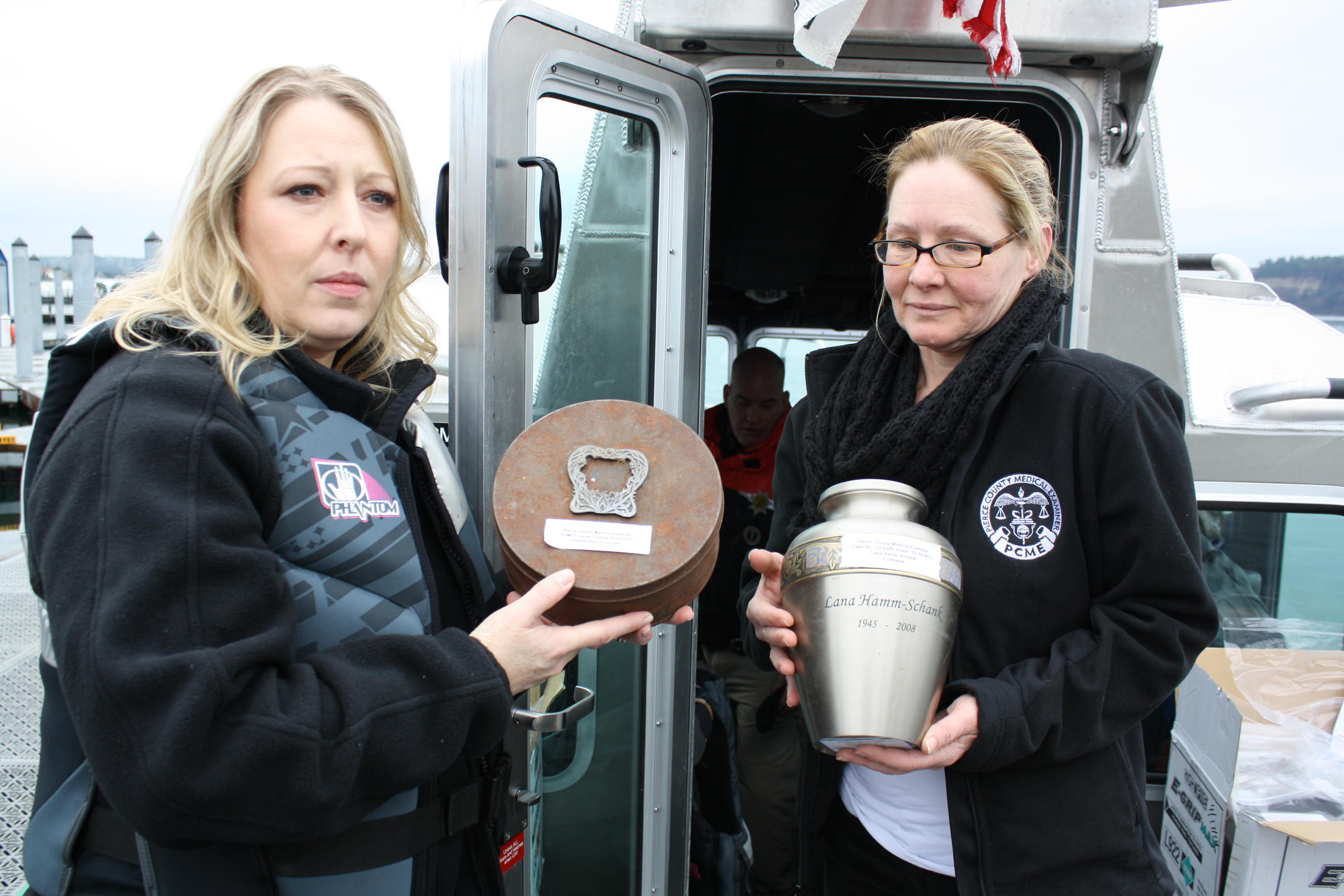 caption: Amber Larkins and Terry Jaeger of the Pierce County Medical Examiner's office hold up vessels containing unclaimed cremated remains.