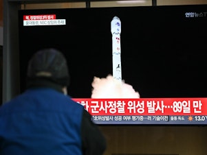caption: A man watches a television screen showing a news broadcast with a picture of North Korea's latest satellite-carrying rocket launch, at a railway station in Seoul on Nov. 22.
