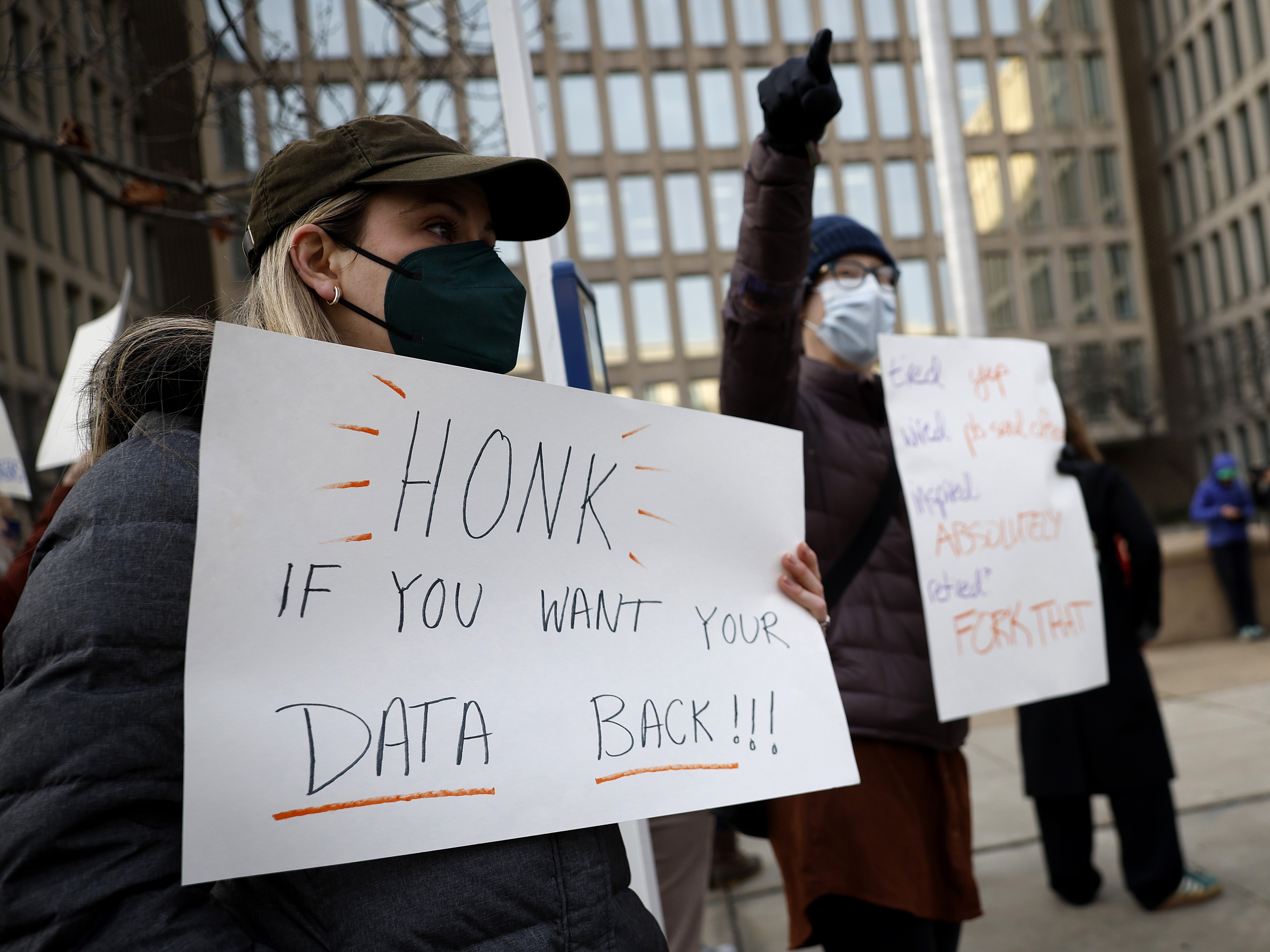 caption: A protester with a sign saying "HONK IF YOU WANT YOUR DATA BACK!!!" stands with other demonstrators outside of the U.S. Office of Personnel Management's headquarters in February in Washington, D.C., to rally against the DOGE team set up by President Trump's billionaire adviser Elon Musk getting access to personal data about federal employees.