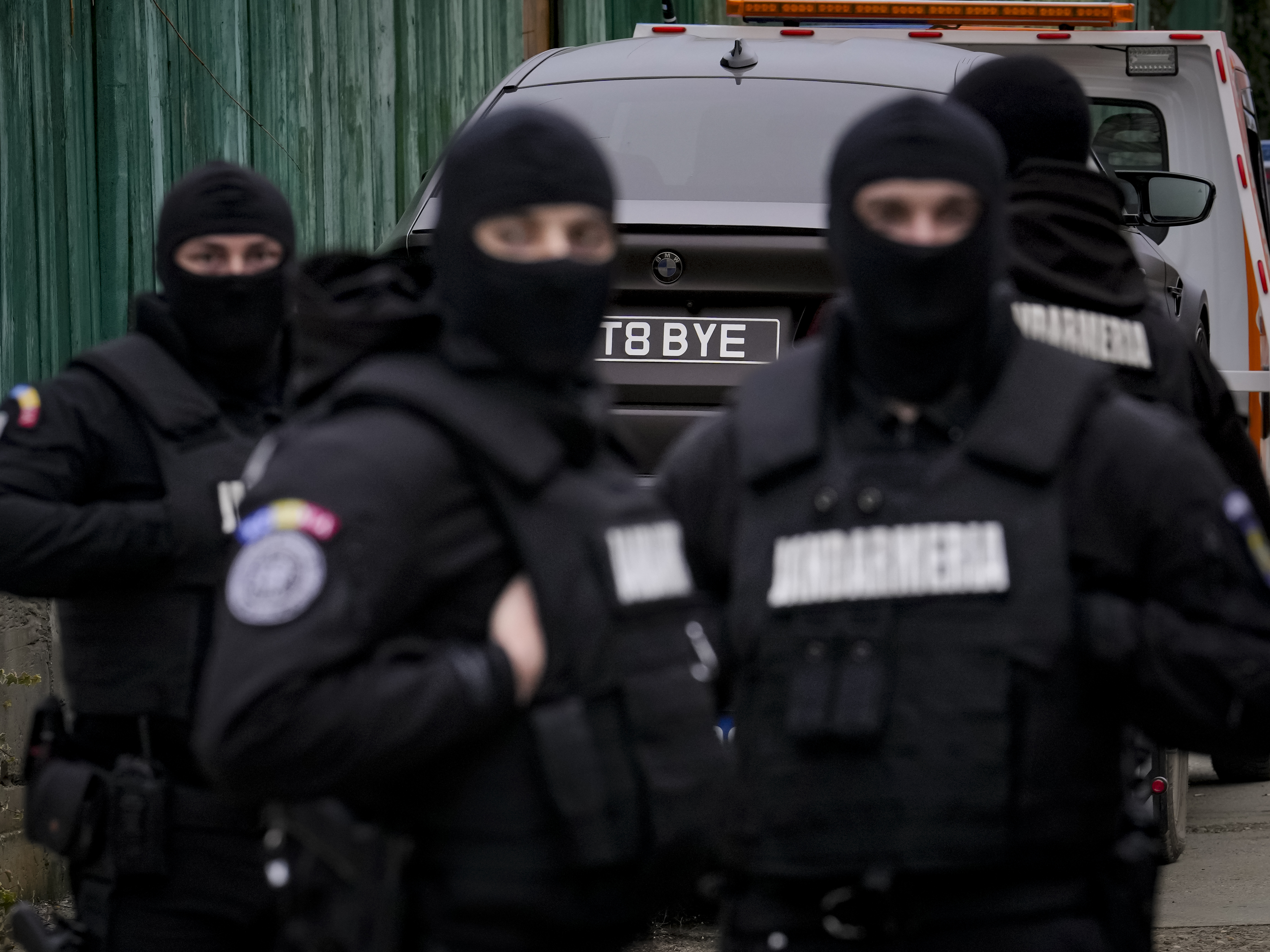 caption: Romanian officials are backdropped by a luxury vehicle which was seized in a case against media influencer Andrew Tate on Saturday, Jan. 14, 2023.
