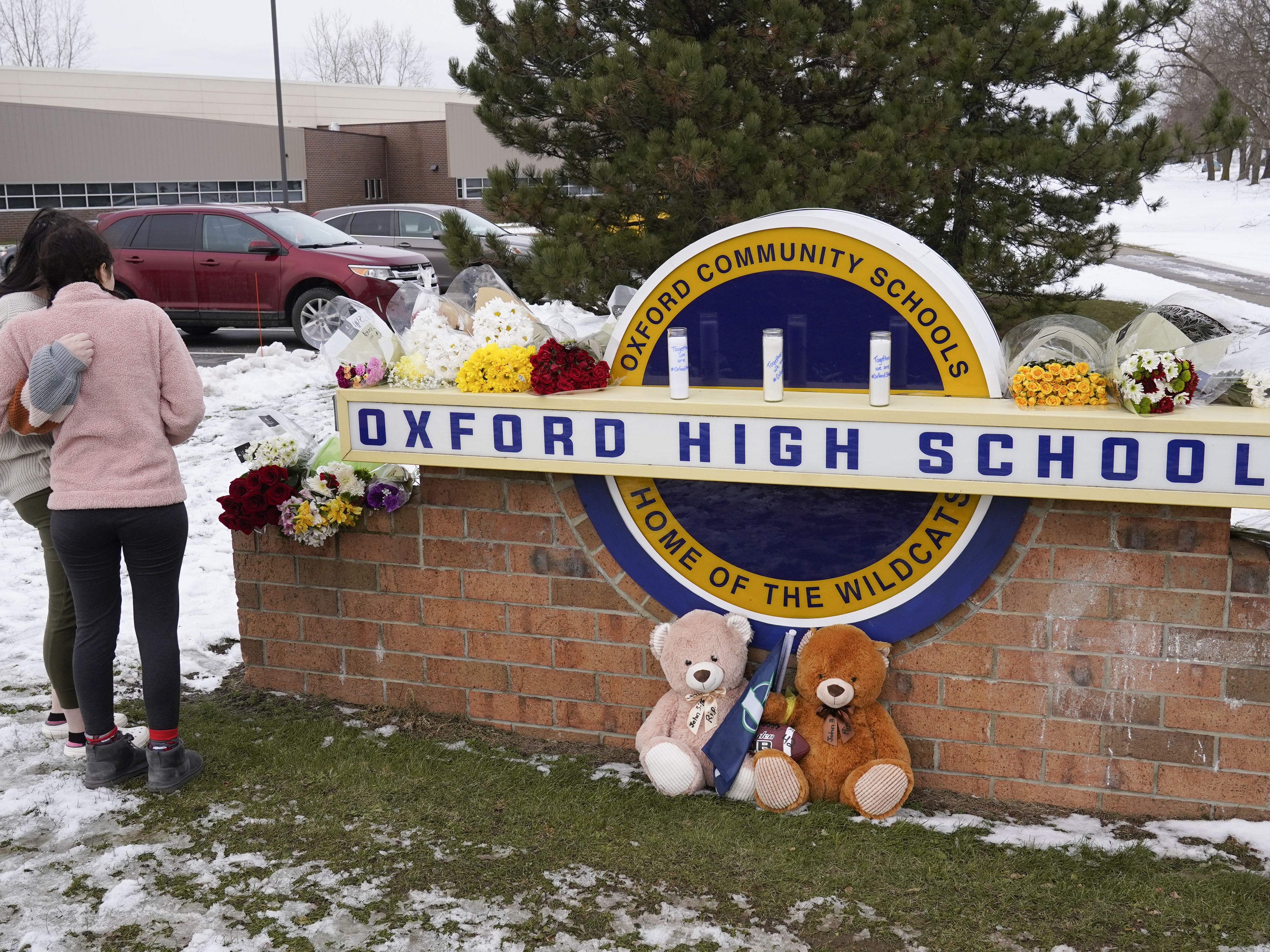 caption: Students stand outside Oxford High School, near memorial items that were placed after the November 2021 shooting that took place at the Michigan school.