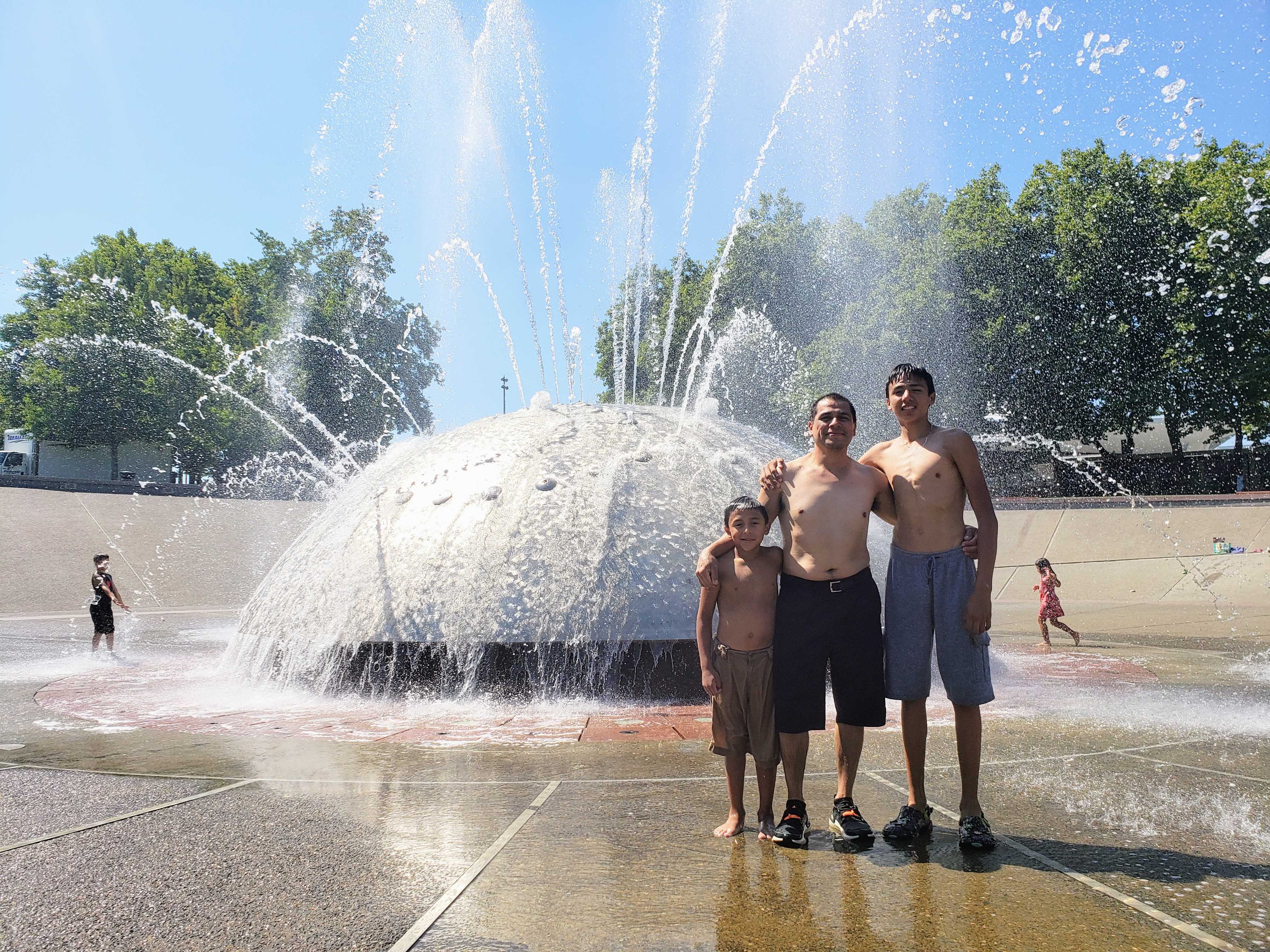 caption: Omar Rodriguez and his sons, Julian and Nathaniel, run through International Fountain on Monday, August 14, 2023.