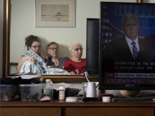 caption: Sophia Lansky, Neil Kramer and Kramer's mother, Elaine, watch the news in March 2020, from their two-bedroom apartment in Queens.