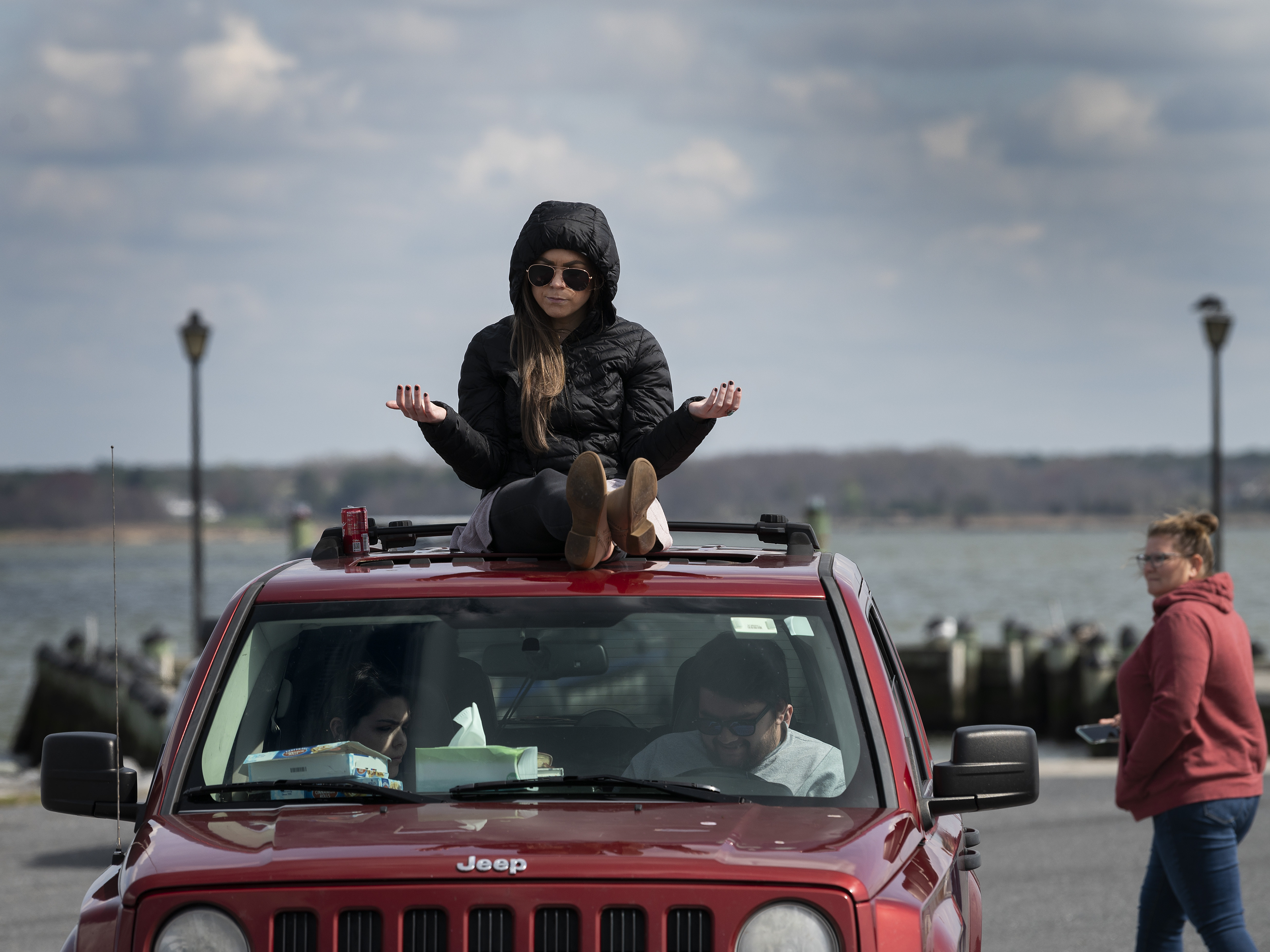 caption: A member of Jesus' Church prays on top of a car during a Sunday church service held at Great Marsh Park in Cambridge, Maryland, on March 22, 2020.