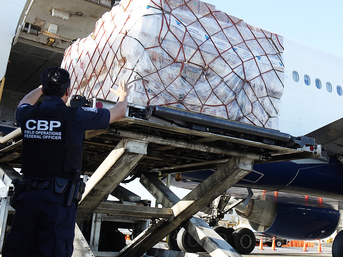 caption: U.S. Customs and Border Protection says it processes some 4 million de minimis shipments every day. Here, CBP officers watch as international shipments are lowered from a plane at Los Angeles International Airport.