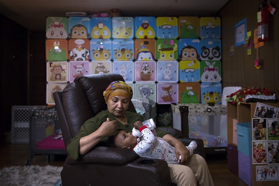 caption: Aqbal Kowaie, an overnight daycare employee holds 10-month-old Avalon Brown before bedtime on Thursday, August 1, 2019, in Renton.