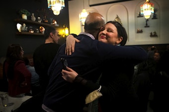 caption: Amy Madden, a member of the Washington State Democratic Party’s executive committee, right, and Faheem Khan, who leads the American Muslim Advancement Council, left, share a hug during a gathering to celebrate the efforts of those who worked to secure uncommitted delegates to send a message to President Biden to call for a permanent ceasefire in Gaza, on Tuesday, March 12, 2024, at Tanoor in Seattle. 