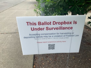 caption:  Signs like this one at the Broadview library branch in north Seattle popped up at some King County ballot drop boxes in July. They prompted concerns about voter intimidation and ultimately an investigation by the King County Sheriff's Office. 