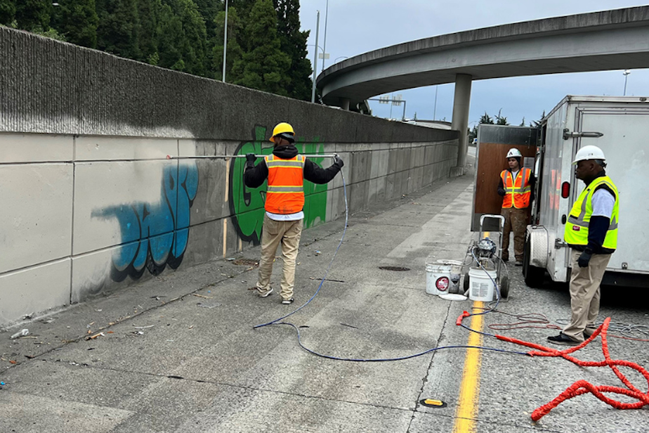 caption: Crews hired by the Washington State Department of Transportation remove and paint over graffiti along southbound I-5 through Seattle during "revive I-5" repairs in July 2022. 