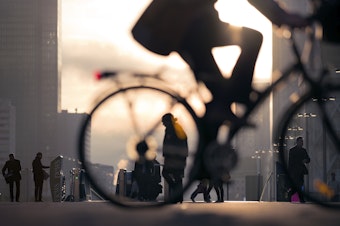 Morning image of businessman biking to work on a bicycle passing skyline of La Defense business district in Paris, France. He is in silhouette against an early morning sky.