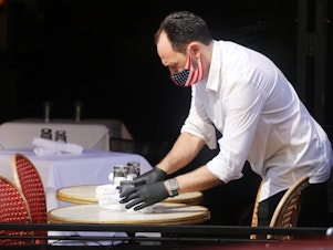caption: A restaurant server in New York prepares a table.