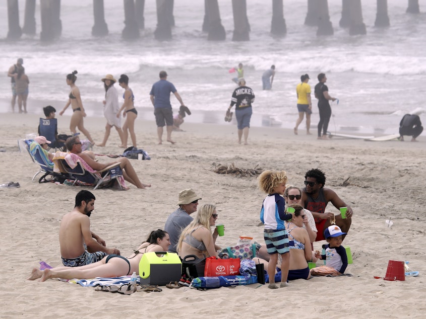 caption: People enjoy a day out on Sunday in Huntington Beach, Calif. High numbers of beachgoers over the weekend prompted warnings from officials that defying stay-at-home orders could reverse progress and bring the coronavirus surging back.