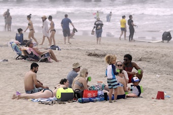 caption: People enjoy a day out on Sunday in Huntington Beach, Calif. High numbers of beachgoers over the weekend prompted warnings from officials that defying stay-at-home orders could reverse progress and bring the coronavirus surging back.
