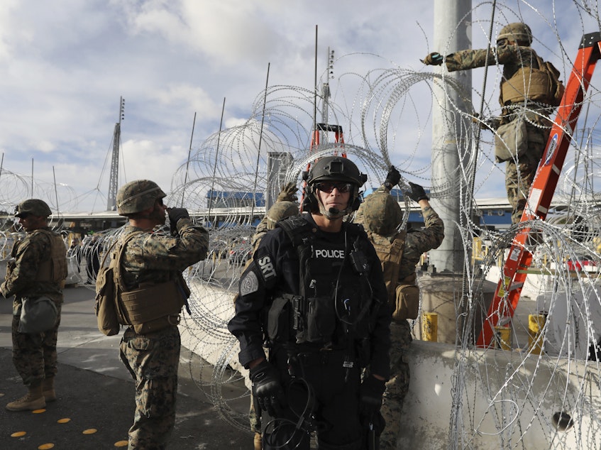 caption: Troops set up concertina wire as a Customs and Border Protection agent stands guard on the U.S. side of the border with Mexico, on Thanksgiving Day.