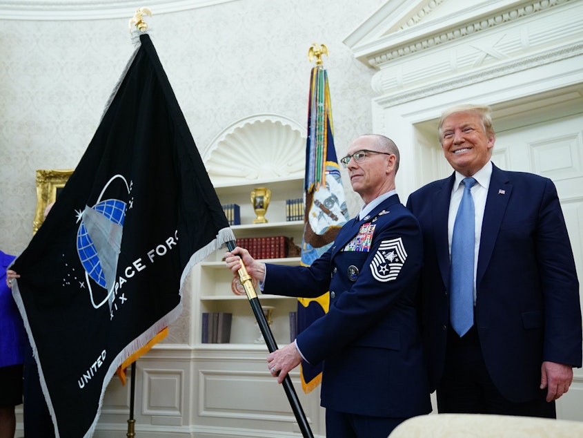 caption: U.S. Space Force Senior Enlisted Advisor CMSgt Roger Towberman, standing with President Trump, presents the Space Force Flag in the Oval Office on March 15.