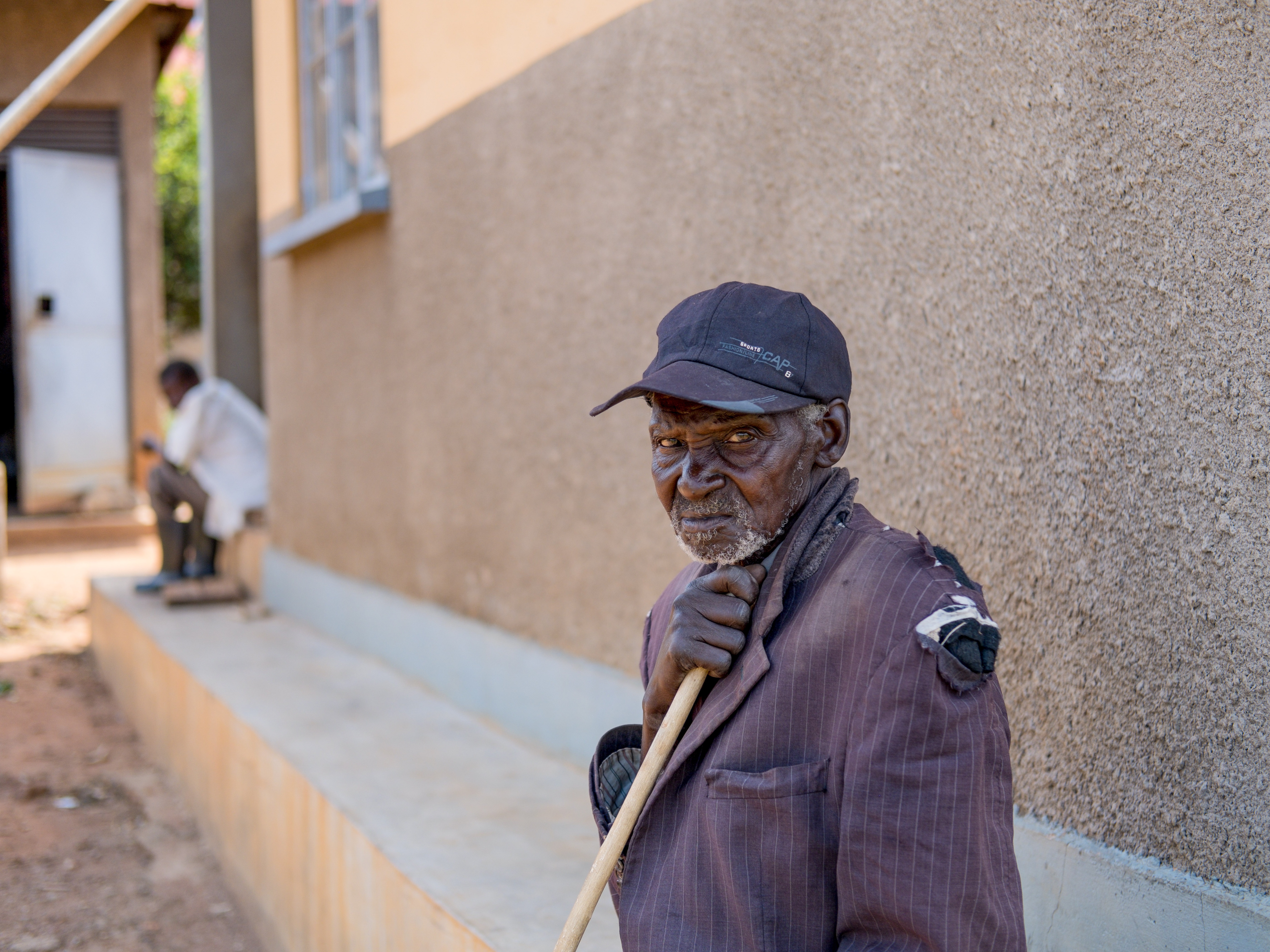 caption: Ukura Midar, 88, had to leave his family's house in 2017 because of construction for a new pipeline project. Now living in a settlement called Kyakaboga, 15 miles from the place he had called home for decades, he says that he is cut off from the graves of several family members, including three of his children, which lie behind a fence.