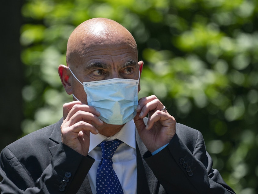 caption: Moncef Slaoui, chief scientific adviser for Operation Warp Speed, listens as President Trump delivers remarks about coronavirus vaccine development in the Rose Garden on May 15. Slaoui says Americans could start seeing a vaccine by the middle of December.