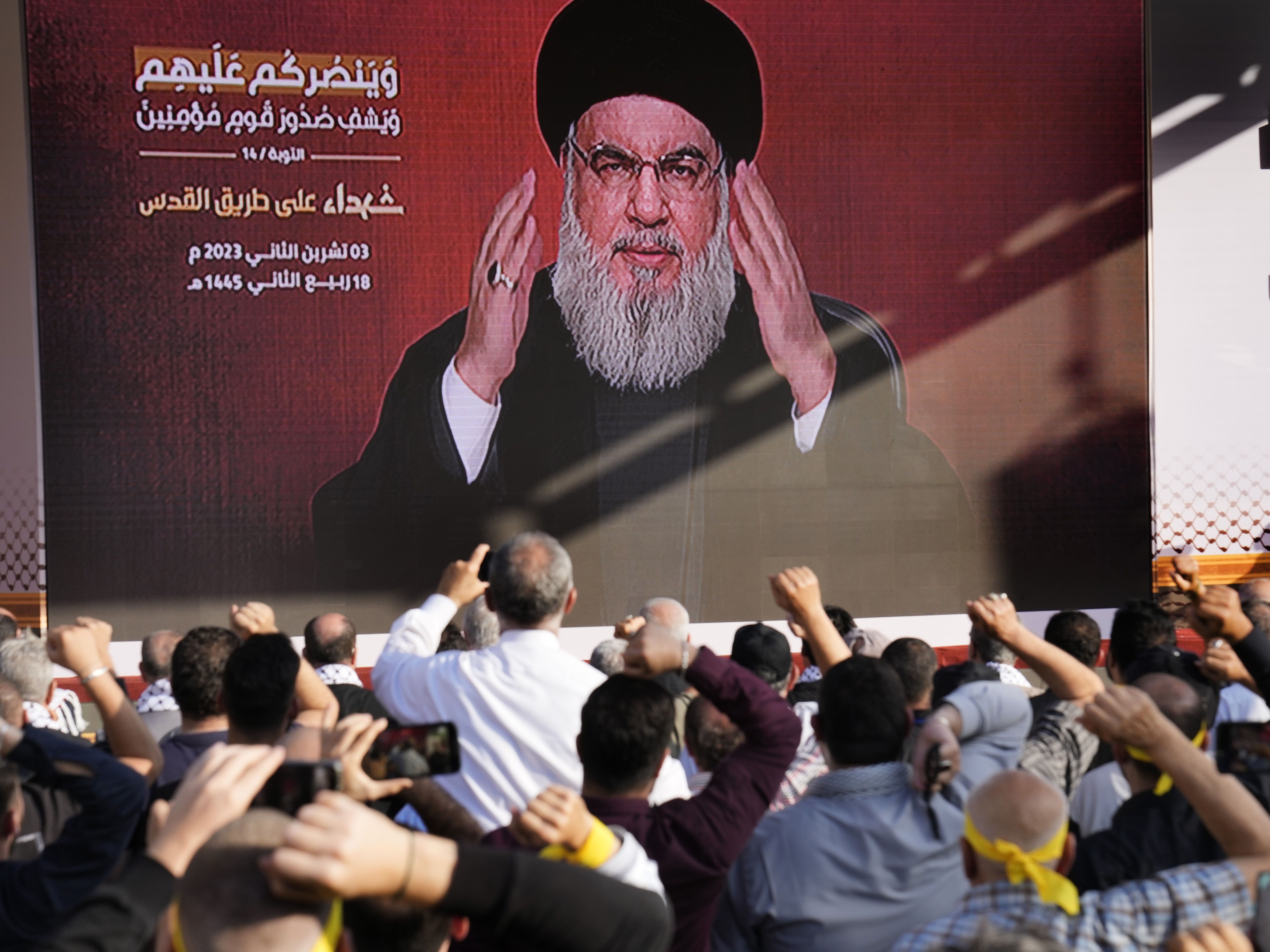 caption: Supporters of the Iranian-backed Hezbollah group raise their fists and cheer as Hezbollah leader Hassan Nasrallah appears via a video link, during a Nov. 3, 2023, rally in Beirut to commemorate Hezbollah fighters who were killed in South Lebanon while fighting against the Israeli forces.