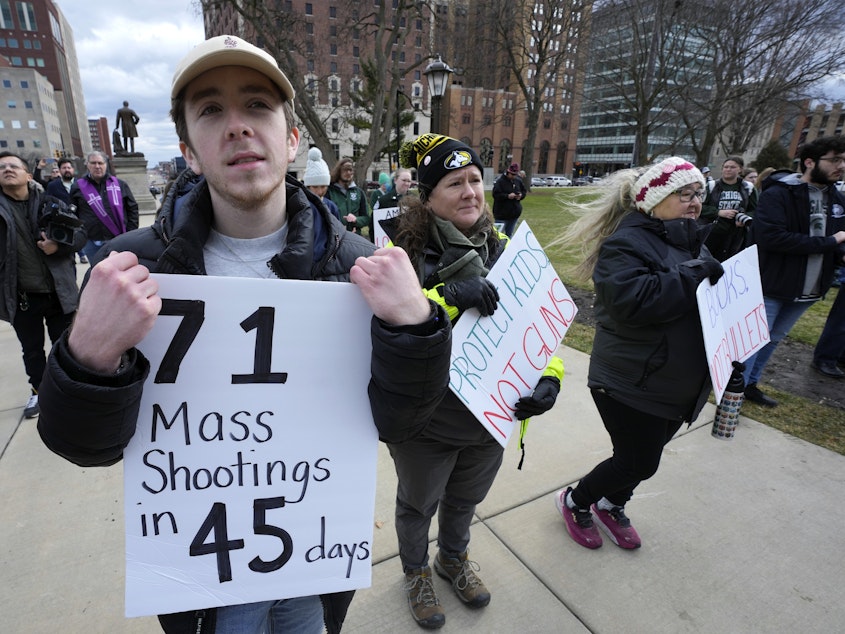 caption: Austin Hunt holds a sign with current and former Michigan State University students during a rally at the state Capitol in Lansing, Mich., Wed., Feb. 15, 2023, after a gunman opened fire on the Michigan State University campus Monday night.