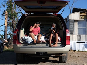 caption: Carlos and Jessica Deviana sit in the back of their father's SUV, which they were using as a bedroom after Hurricane Michael destroyed their home in Panama City, Fla., in October 2018.