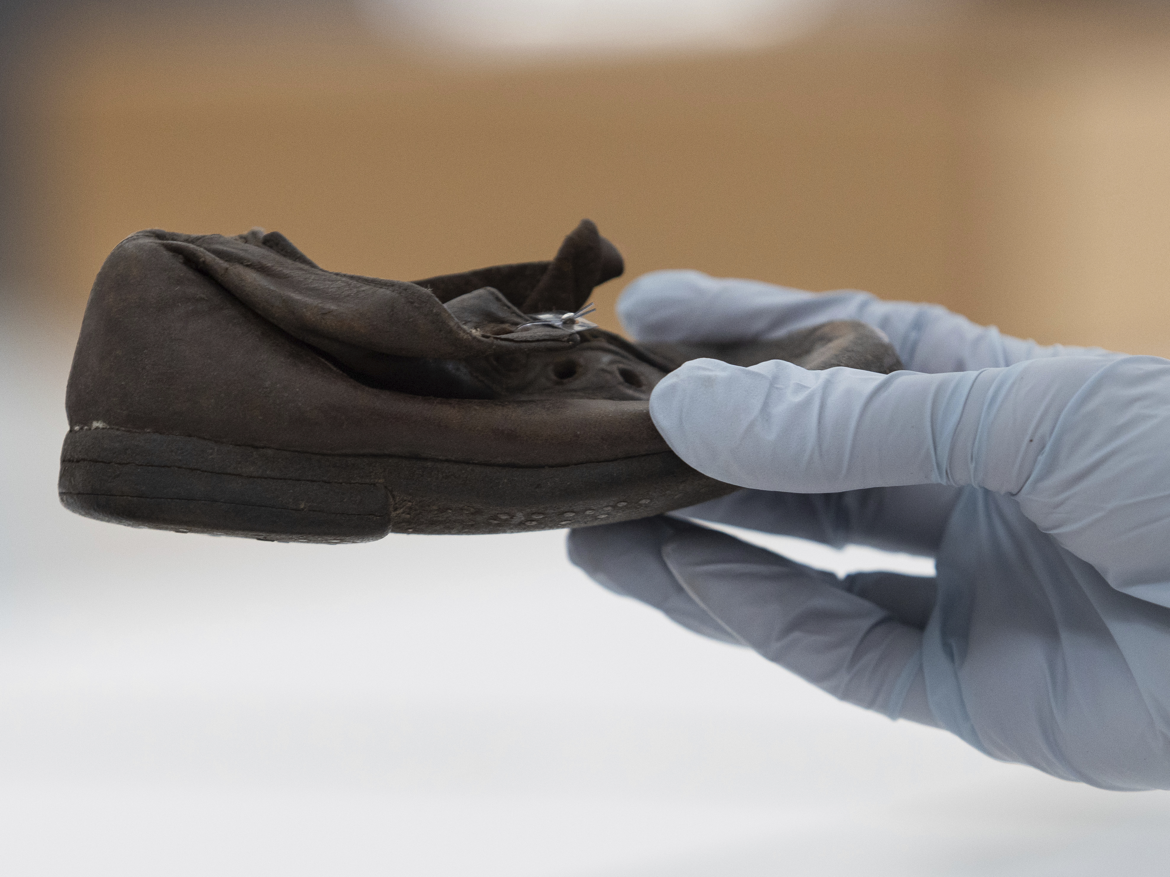 caption: A worker holds a shoe that belonged to a child victim of the former Nazi German death camp Auschwitz-Birkenau at the conservation laboratory on the grounds of the camp in Oswiecim, Poland, Wednesday, May 10, 2023.