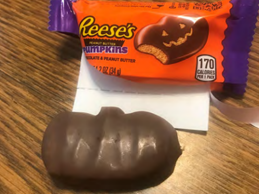 caption: A Reese's Peanut Butter Pumpkin with no carved-out face next to the open wrapper with a jack-o'-lantern design.