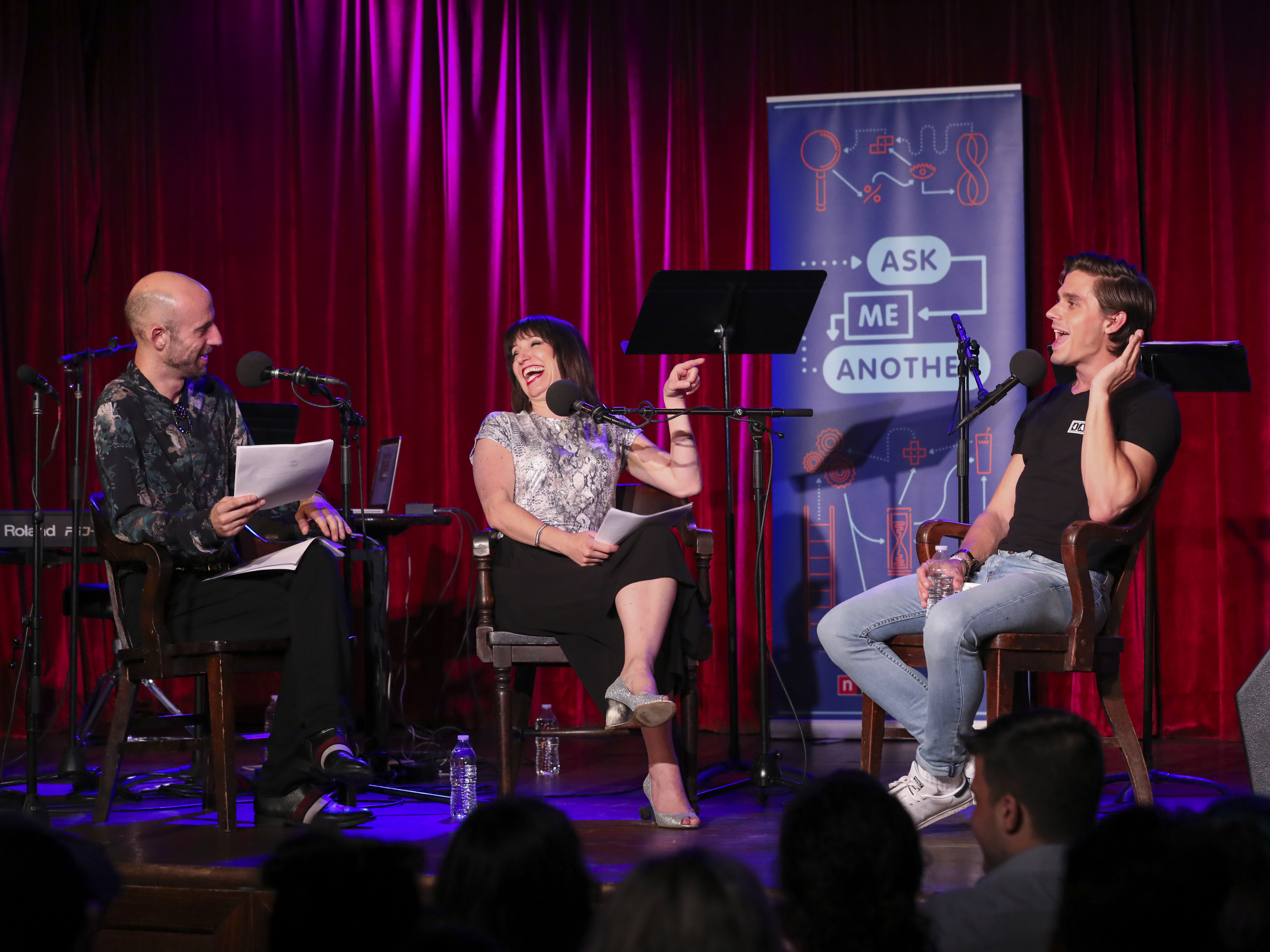 caption: Cecil Baldwin and Ophira Eisenberg lead an <em>Ask Me Another</em> challenge with Antoni Porowski at the Bell House in Brooklyn, New York.