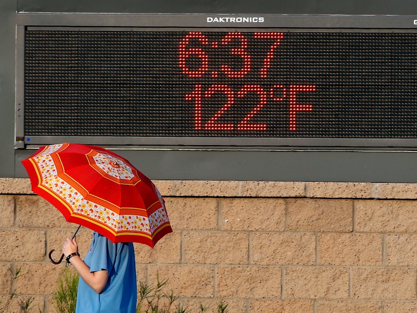 caption: A pedestrian uses an umbrella to get some relief from the sun as she walks past a sign displaying the temperature on June 20, 2017 in Phoenix, Ariz.