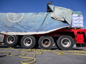 caption: An Egyptian truck driver removes a tarp covering humanitarian aid before it is inspected on its way to the Gaza Strip at the Kerem Shalom Crossing in Israel on Dec. 22, 2023.