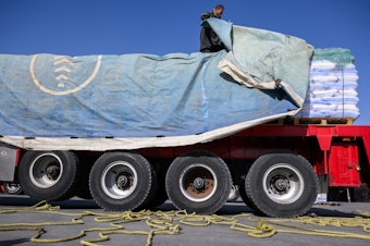 caption: An Egyptian truck driver removes a tarp covering humanitarian aid before it is inspected on its way to the Gaza Strip at the Kerem Shalom Crossing in Israel on Dec. 22, 2023.