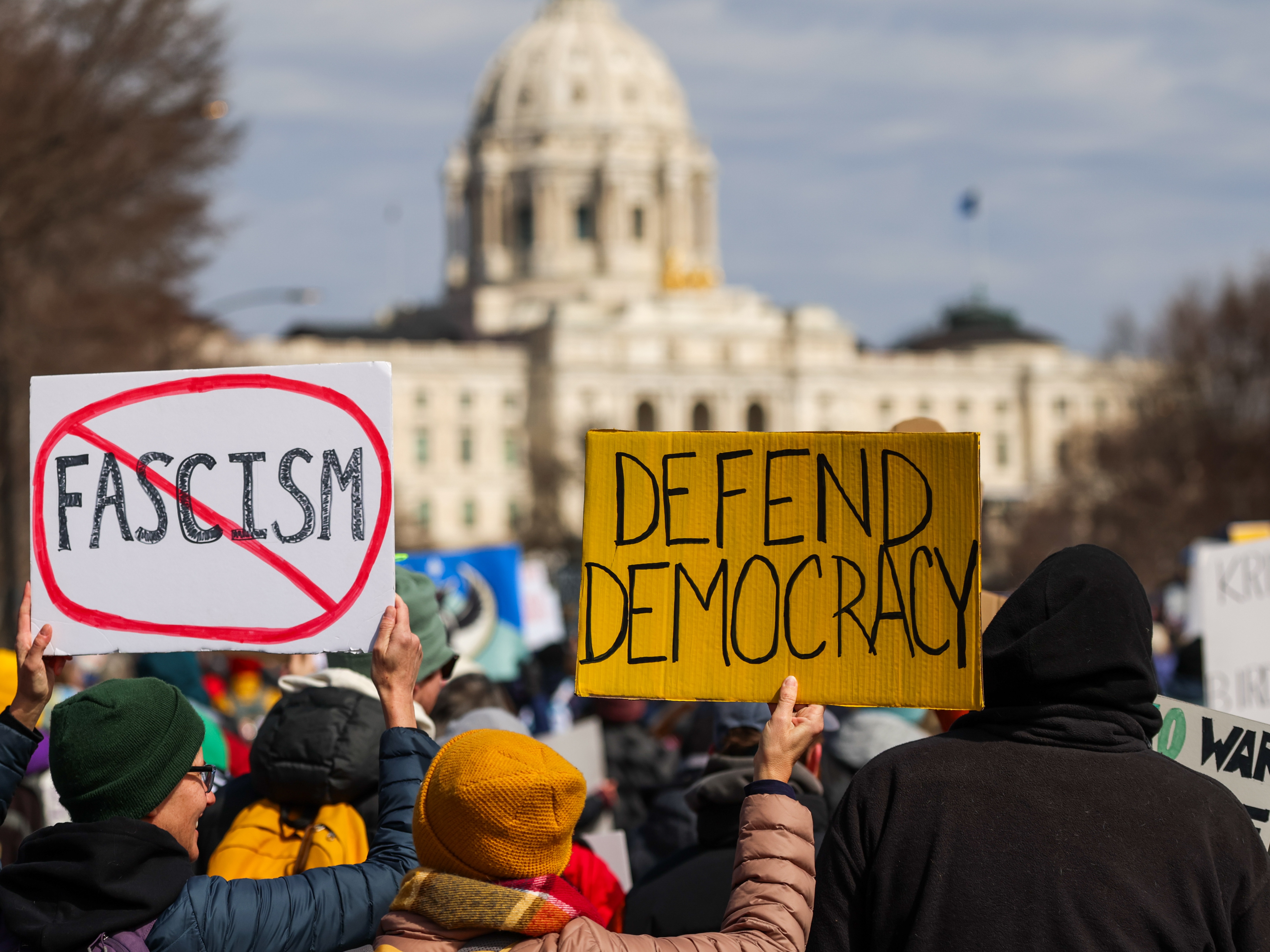 caption: Demonstrators hold signs while marching towards the Minnesota State Capitol during a No Kings protest in St. Paul on Saturday.