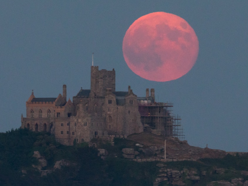 caption: The strawberry moon rises behind St Michael's Mount in Marazion near Penzance on June 28, 2018, in Cornwall, England.