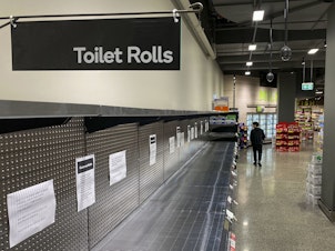 A shopper passes empty shelves usually stocked with toilet paper in a supermarket