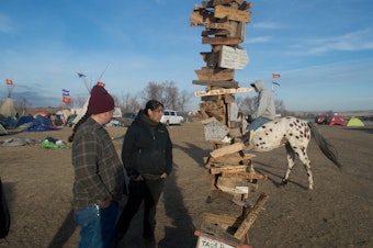 caption: A man rides a horse past a post with signs pointing in all directions, towards the homelands of the thousands of indegnous people who came to Standing Rock. Native people lived there in a way they haven't for hundreds of years. 