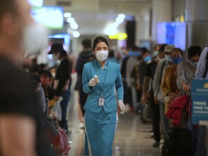 caption: An airline employee holds a thermometer to check boarding passengers at Noi Bai International Airport in Hanoi, Vietnam. After three weeks with no local cases reported, Vietnam has reopened schools, businesses, factories and tourist attractions.