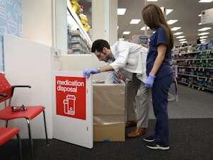caption: CVS Pharmacist Raphael Lynne (left), D., MBA, and Stephanie Garcia, a Pharmacy tech., check the medication disposal box where people can drop off their expired, unused or unwanted medications for safe disposal.