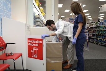 caption: CVS Pharmacist Raphael Lynne (left), D., MBA, and Stephanie Garcia, a Pharmacy tech., check the medication disposal box where people can drop off their expired, unused or unwanted medications for safe disposal.