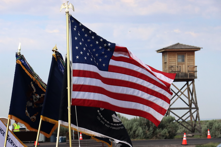 caption: The American flag sways as the replica guard tower towers over pilgrims during the closing ceremony at the Minidoka National Historic Site in rural Idaho.