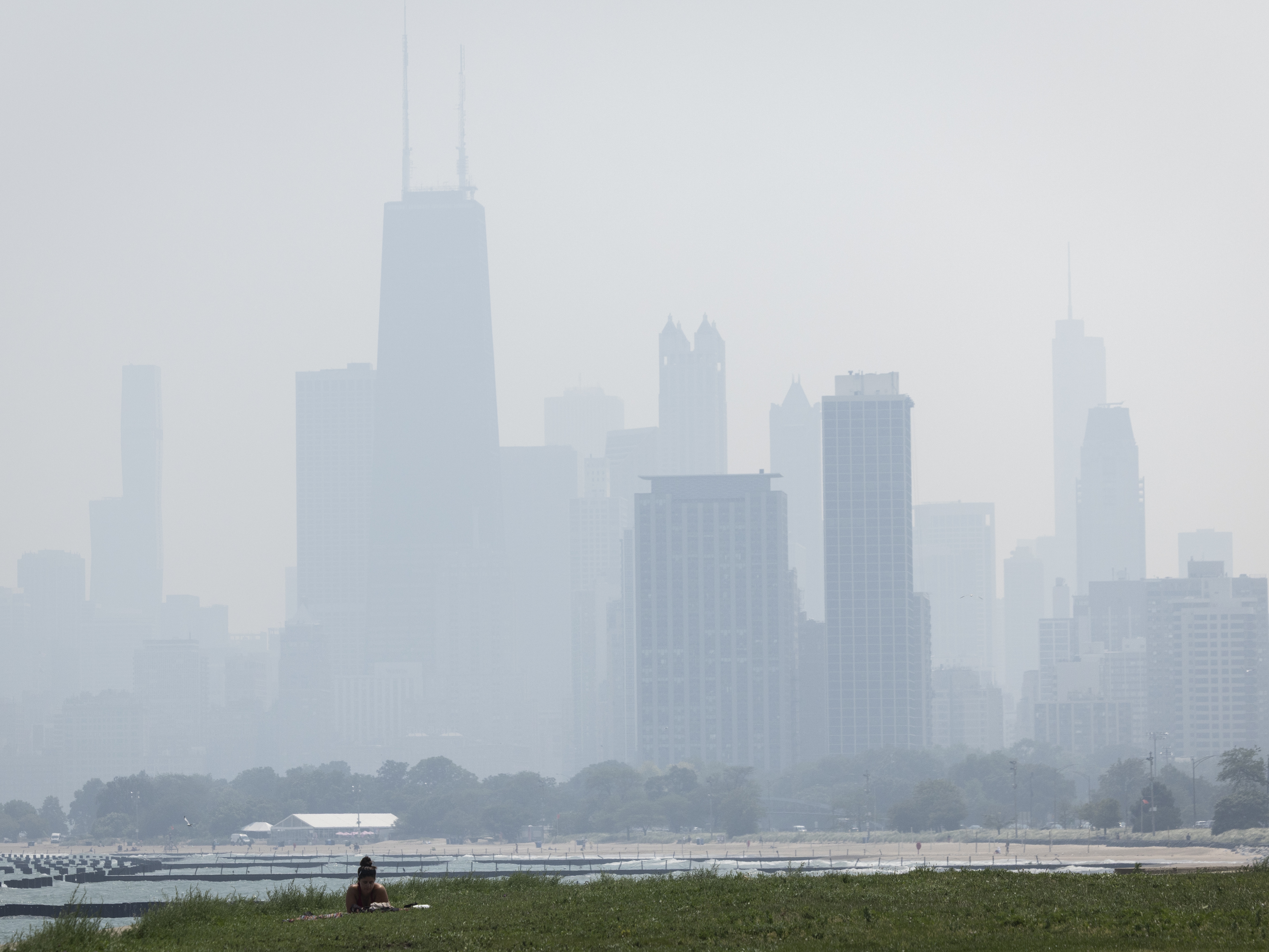 caption: People sun tan in grass off the Lakefront Trail on the North Side as a haze of Canadian wildfire smoke blankets the Chicago area and creates poor air quality, Thursday, July 31, 2025.