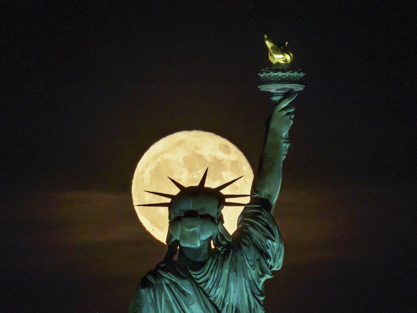 caption: The strawberry supermoon rises in front of the Statue of Liberty in New York on June 14. After July's supermoon on Tuesday there will be one more for the year on Aug. 11.